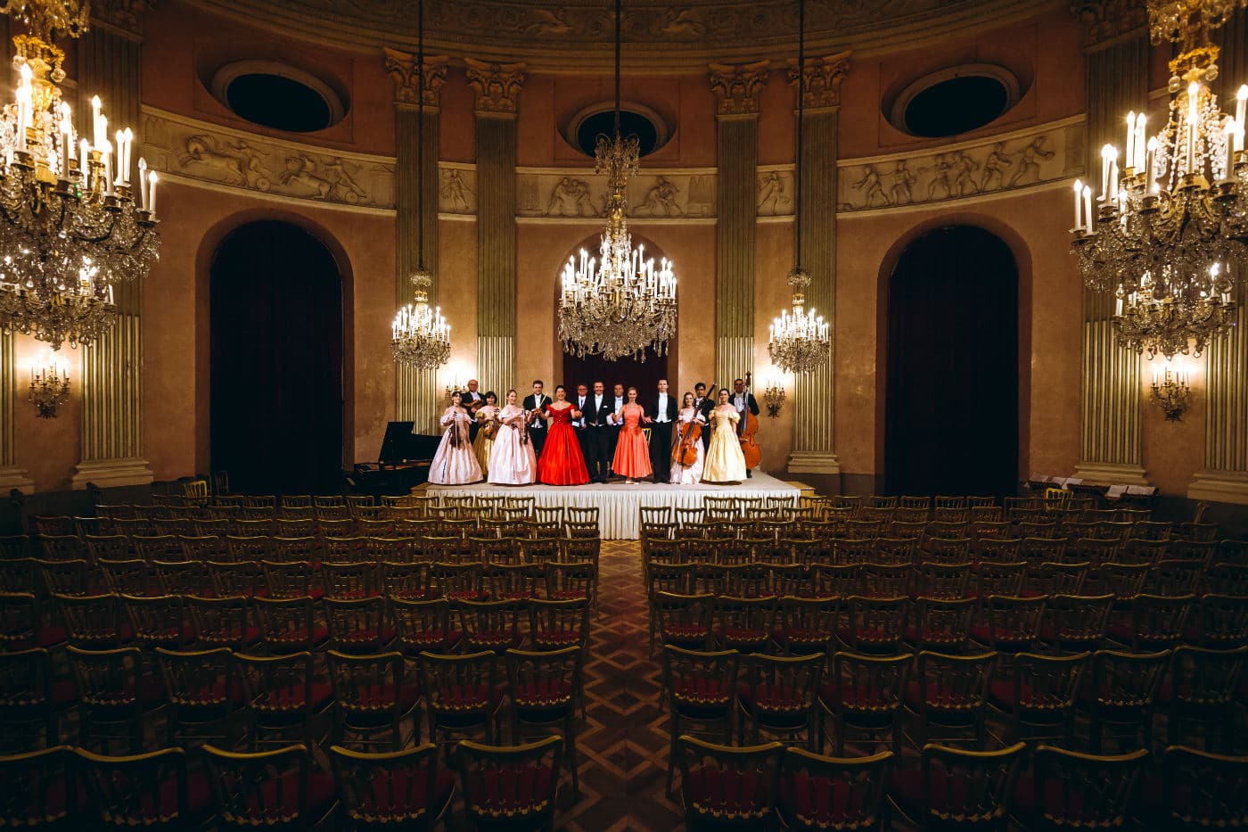 Orchestra e ballerini in abiti da gala sul palco, illuminati da maestosi lampadari durante un concerto classico a Vienna.