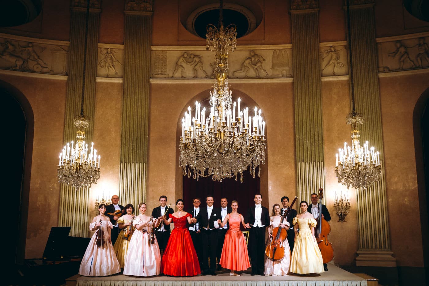 Le Vienna Residence Orchestra et ses solistes saluent sur scène après le concert, sous un lustre imposant dans une salle historique.