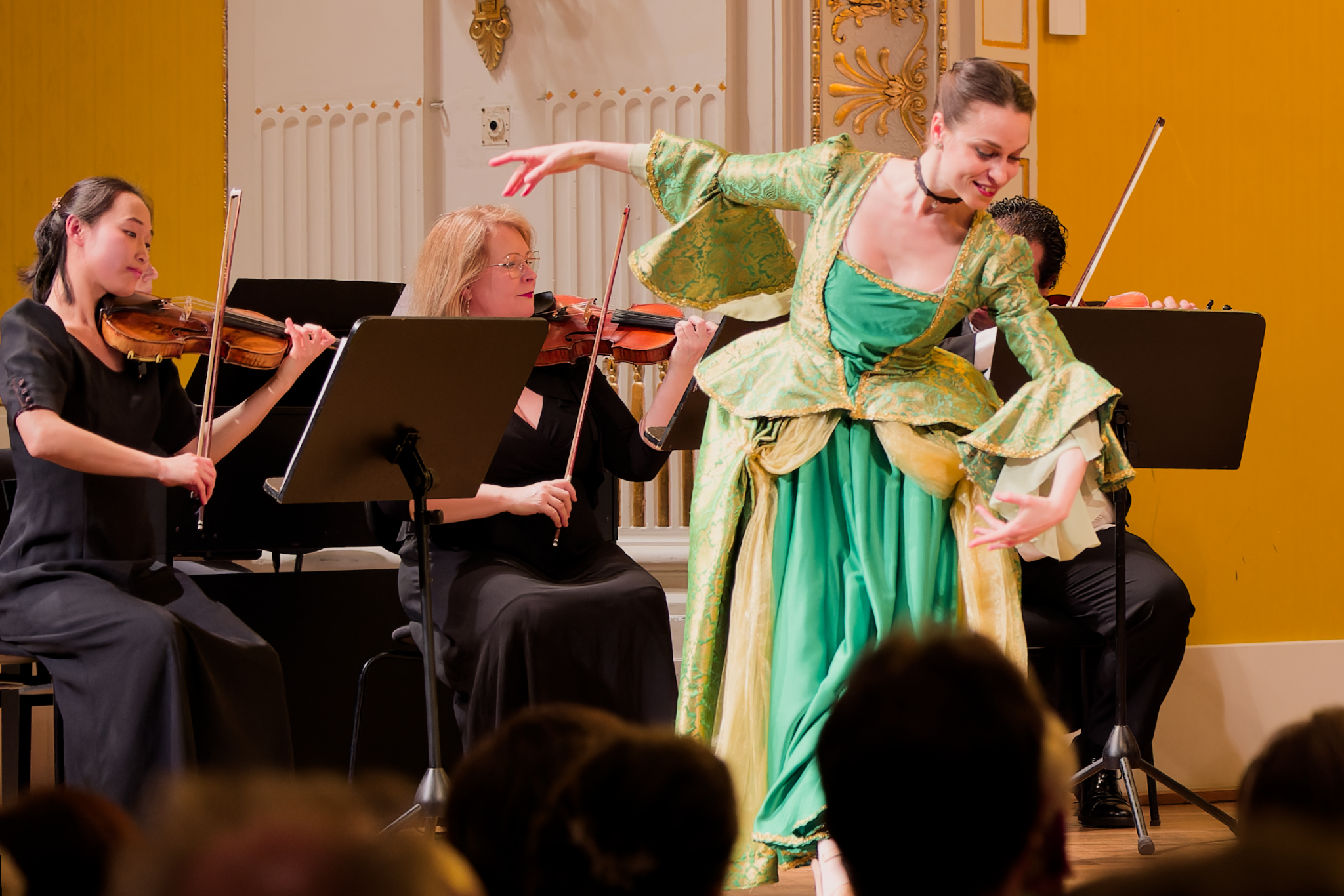 Ballerina in abito verde durante una performance con musicisti d’archi sul palco del Schubertsaal di Vienna.