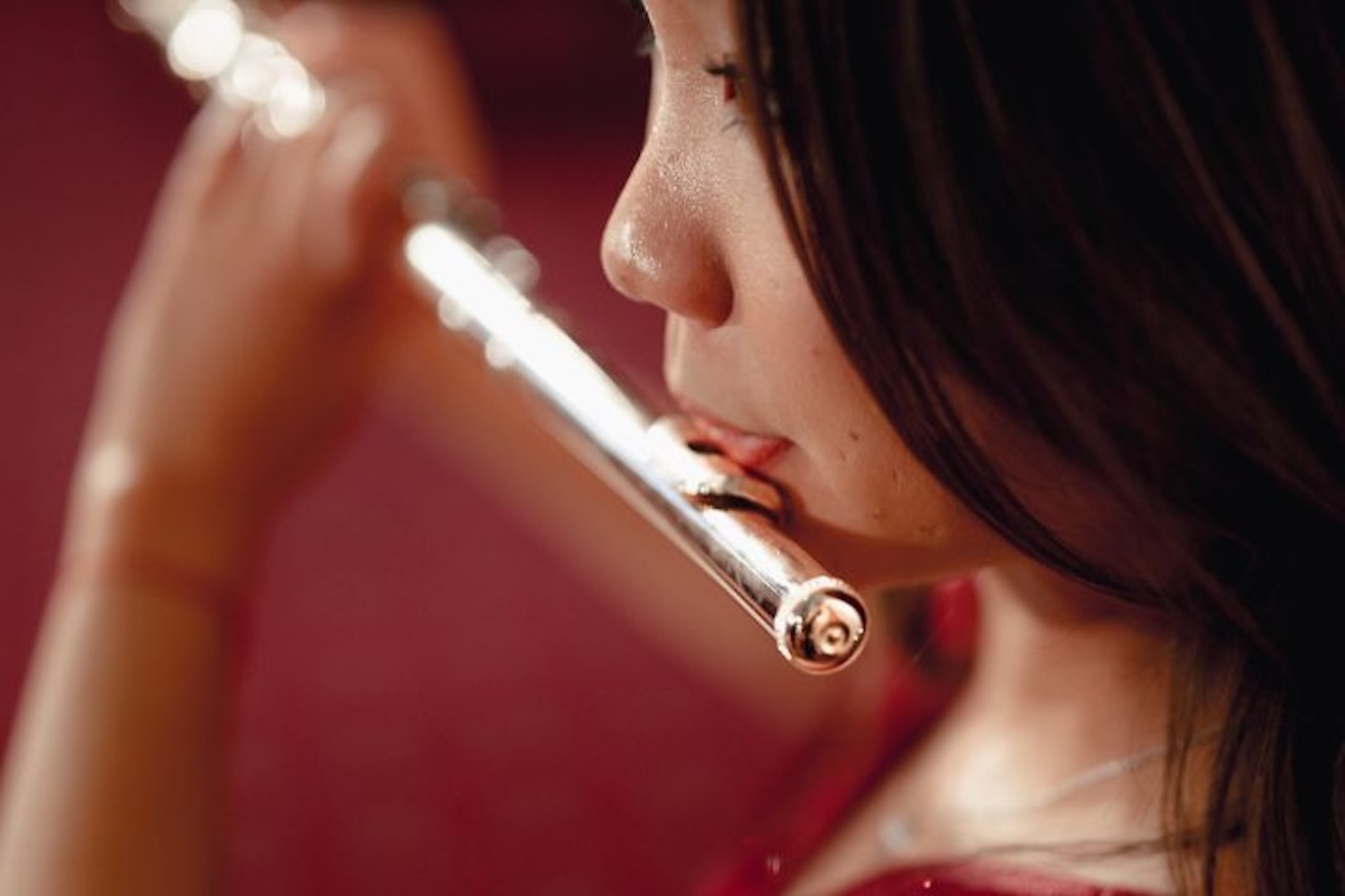 Primo piano di una musicista che suona il flauto traverso con sfondo rosso.