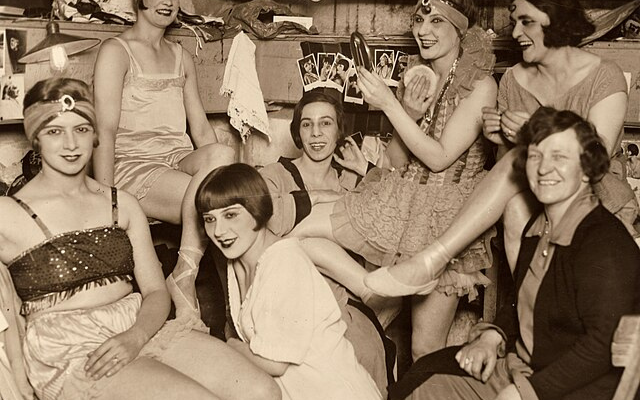 Gruppe junger Frauen in Operettenkostümen, lachend und entspannt in der Garderobe.