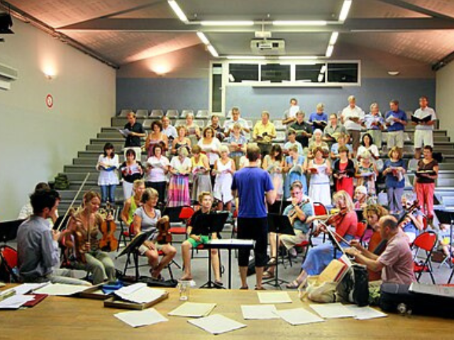 3 Musikstudierende bei einer gemeinsamen Probe mit Chor und Instrumentalisten in einem Übungssaal